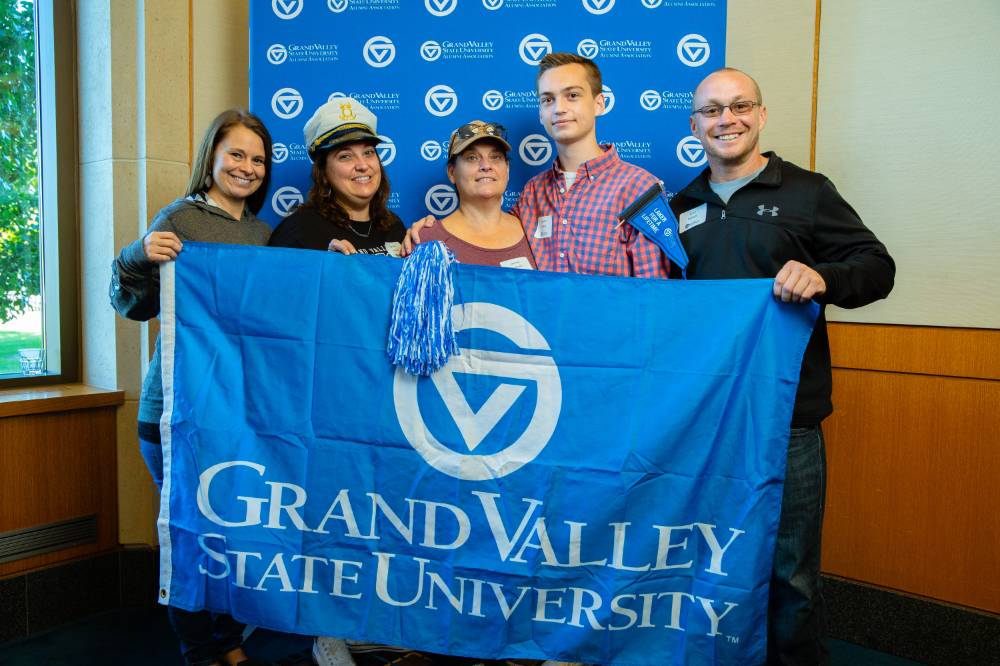 Five alumni pose for a photo while holding on to the GV flag